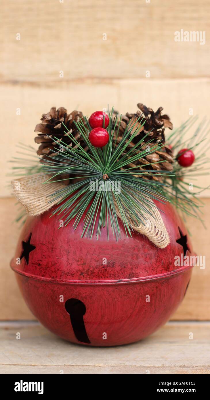 Rosso grande jingle bell decorate con cono di pino, bacche e rafia prua verticale su un legno naturale con uno sfondo con spazio di copia Foto Stock
