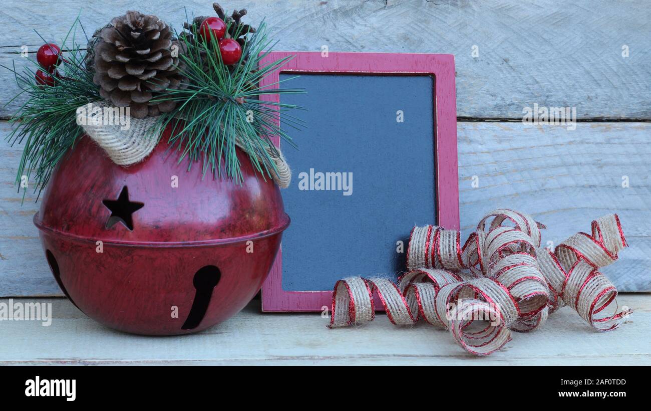 Campanello rosso rustico con stelle intagliate e cono di pino a forma di chiave, nastro verde e lavagna su uno sfondo di legno con spazio di scrittura Foto Stock