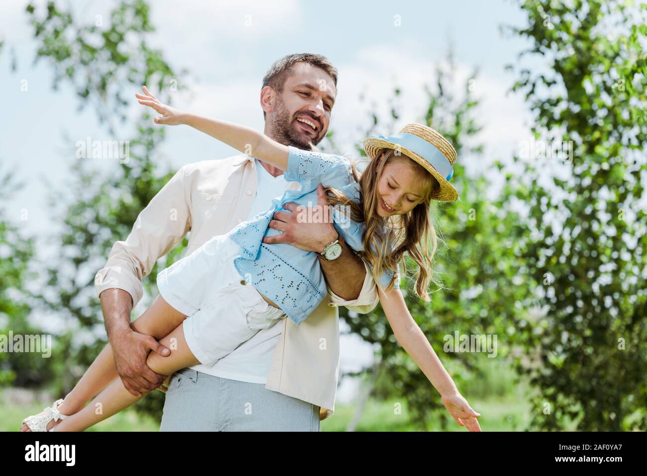 Allegro padre tenendo in bracci figlia felice nel cappello di paglia Foto Stock