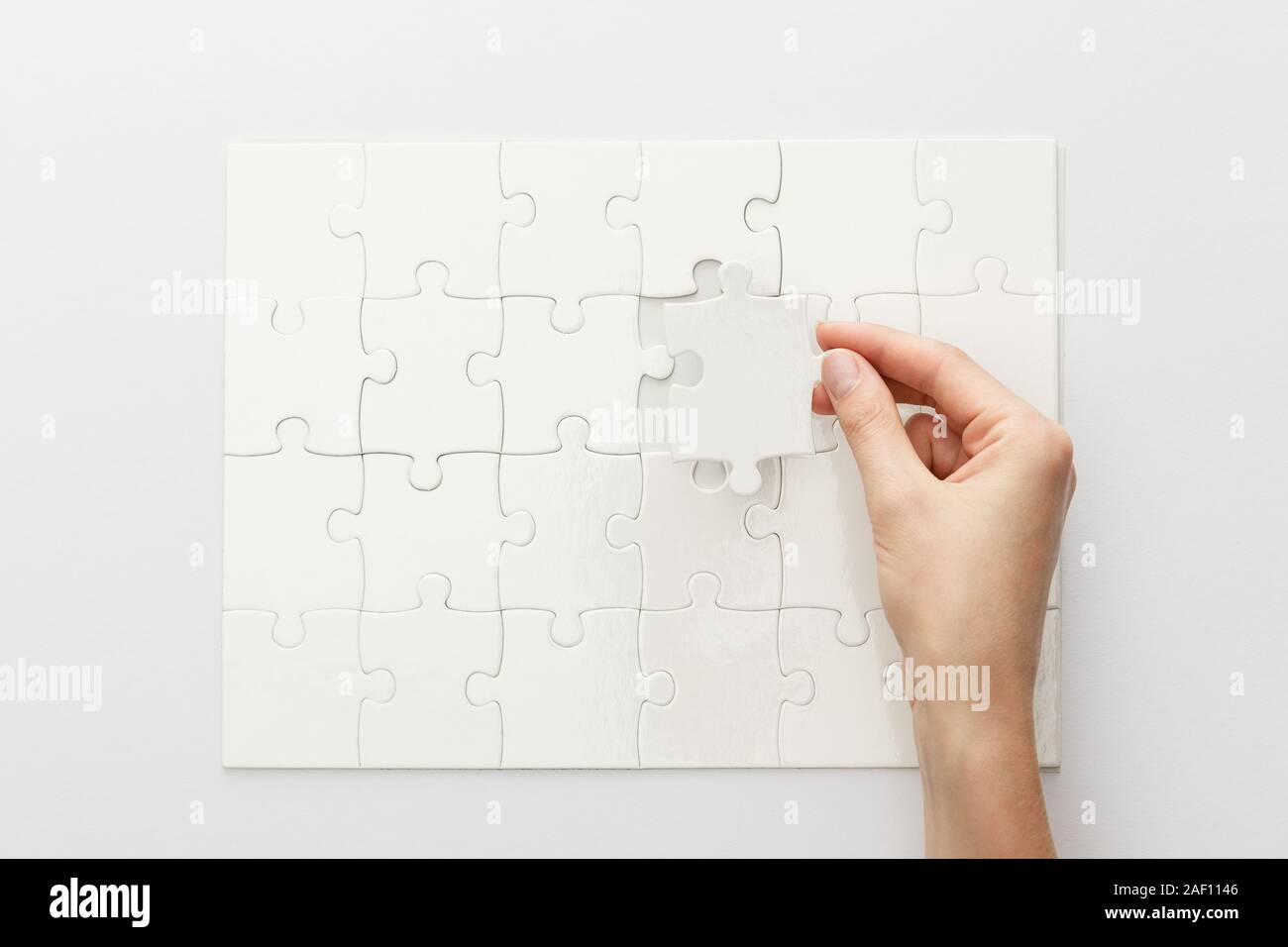 Vista ritagliata della donna completando puzzle su sfondo bianco Foto Stock