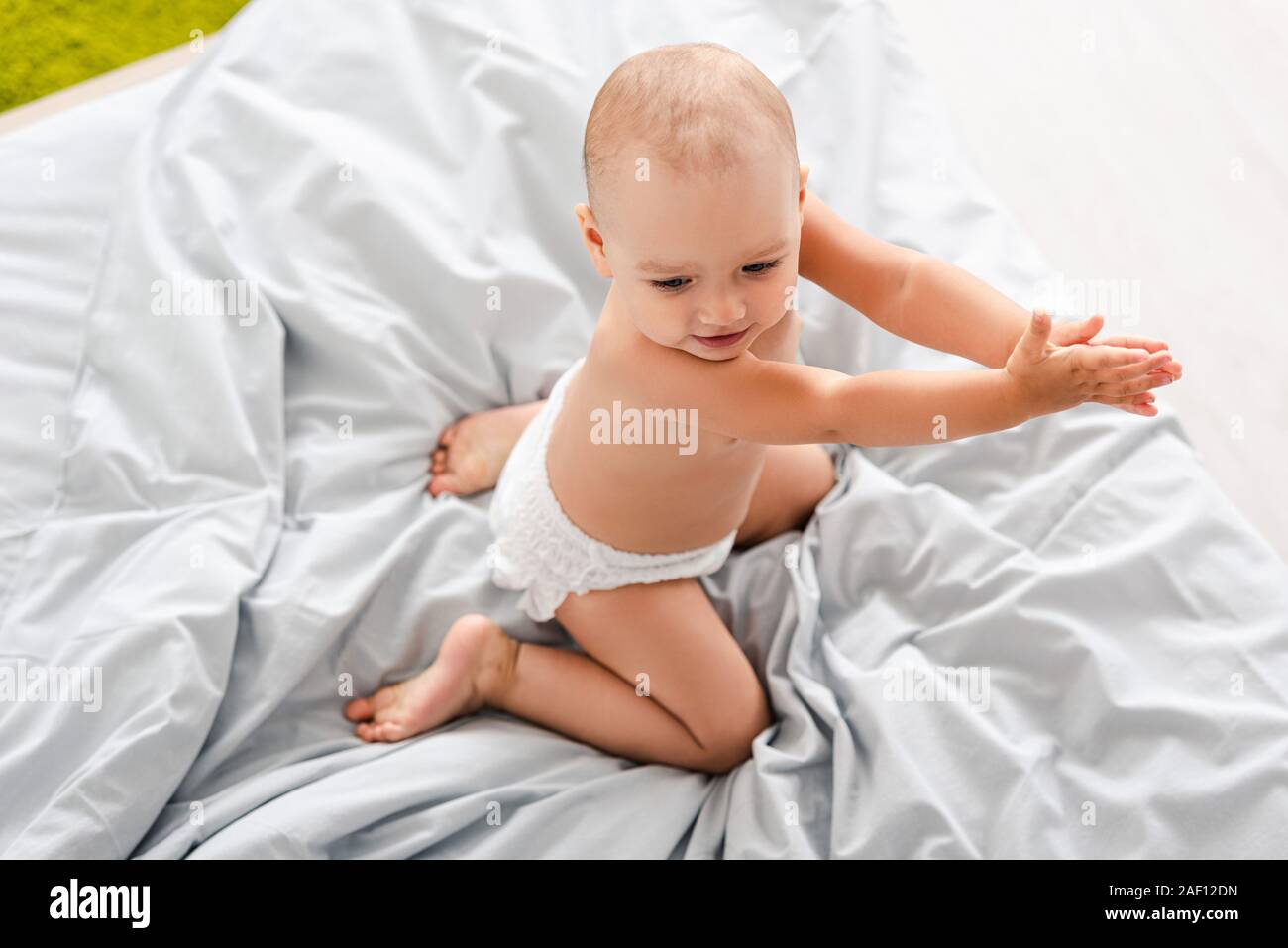 Vista superiore del bambino nel pannolino seduta sul letto e battendo le mani Foto Stock