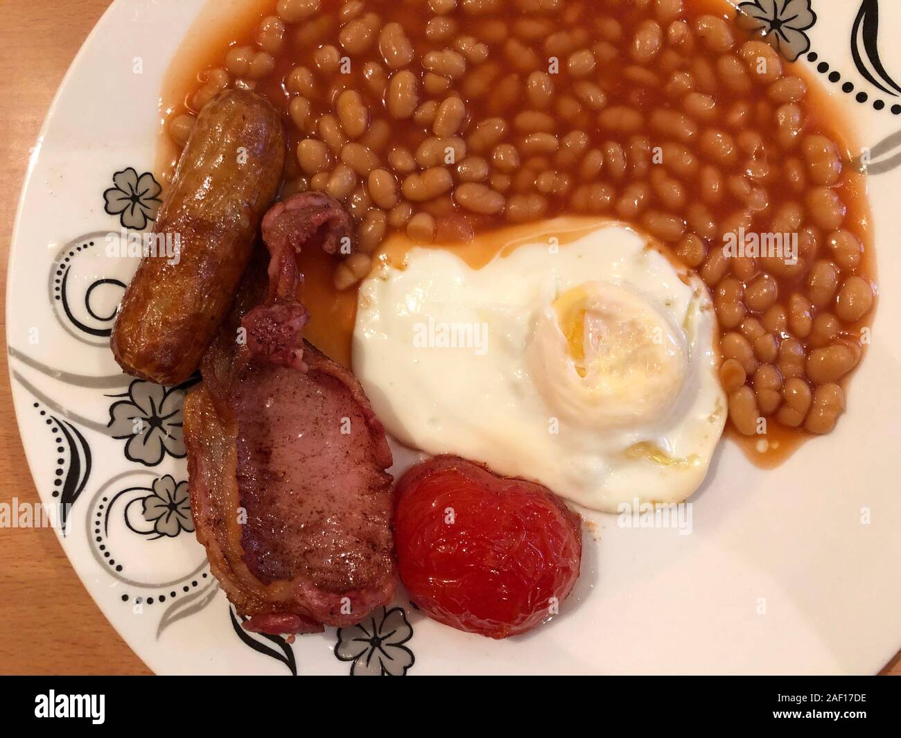Colazione inglese completa tradizionale con uova fritte, fagioli al forno, pancetta, salsiccia e pomodoro al forno in un piatto Foto Stock