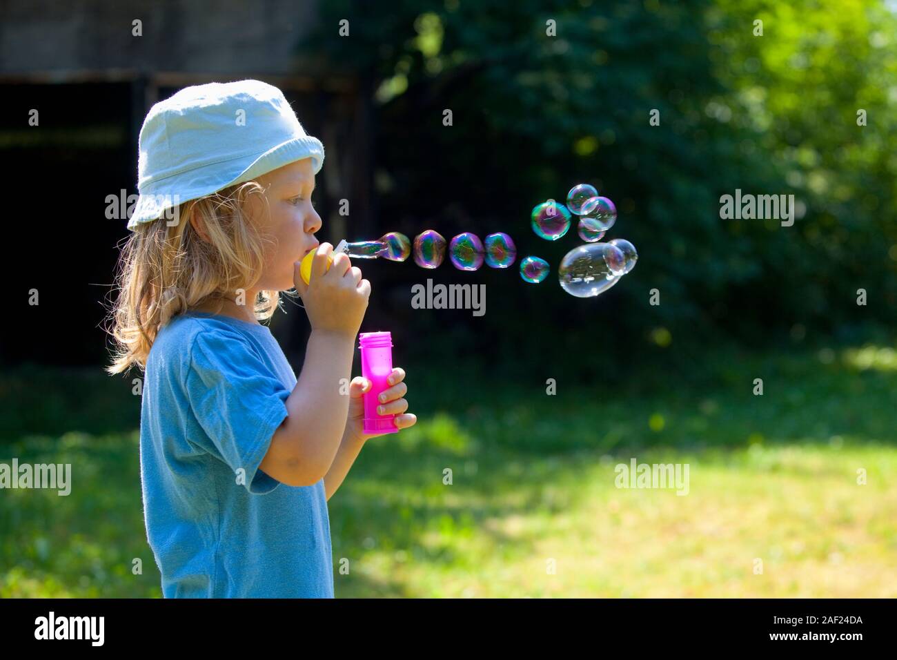 Ragazzo con capelli lunghi biondi soffiando bolle di sapone all'aperto Foto Stock