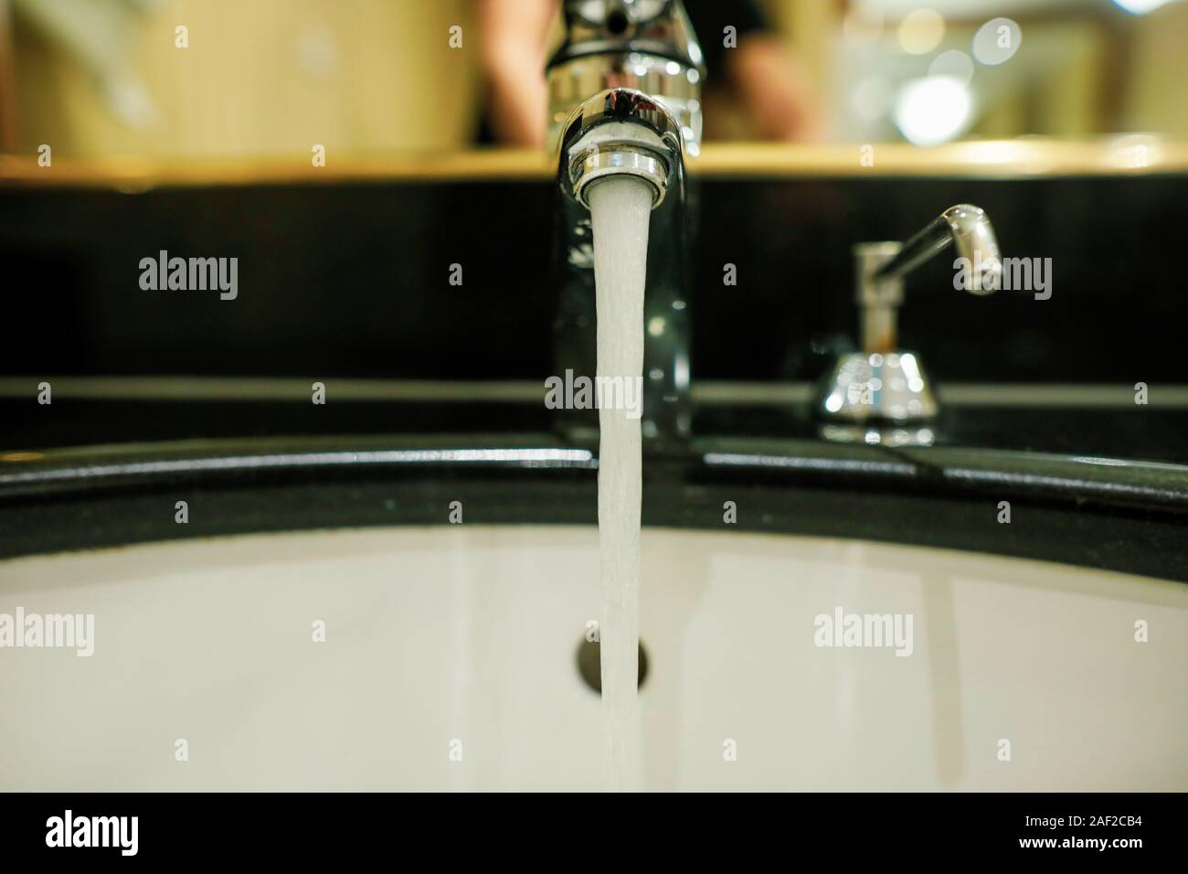 Profondità di campo (messa a fuoco selettiva) immagine con acqua che scorre da un rubinetto e un dispensatore di sapone in un bagno di hotel. Foto Stock