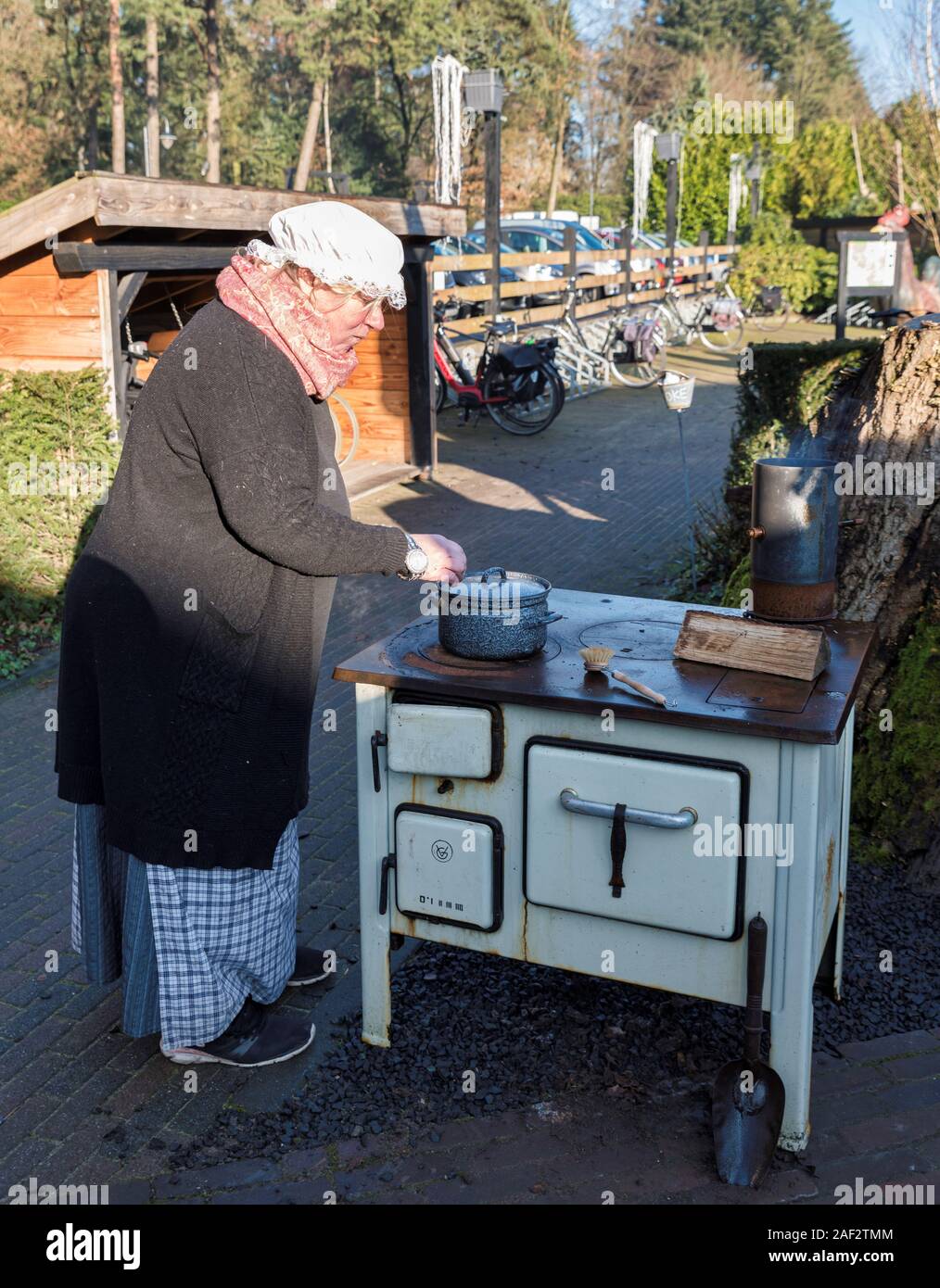 Garderen,Olanda,04-12-2019: una donna è una cottura in pentola in ceramica su una vecchia stufa a legna durante un winterfair in garderen Foto Stock