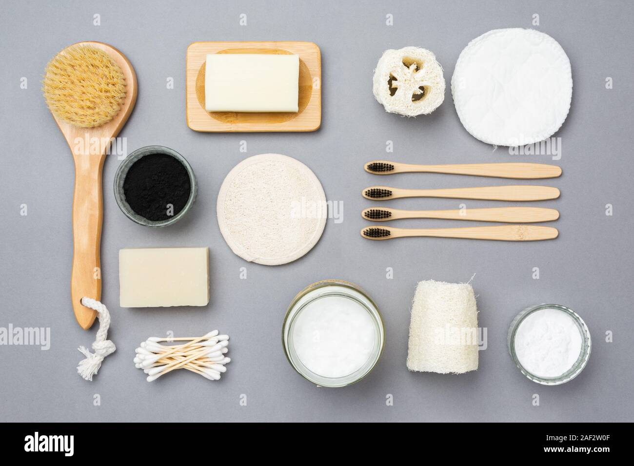 Rifiuti Zero eco friendly prodotti per la cura personale delle spazzole in legno, bambù spazzolini da denti, la Luffa, saponi naturali; olio di noce di cocco, activatd carbone, soda su sfondo grigio, vista dall'alto, il fuoco selettivo Foto Stock