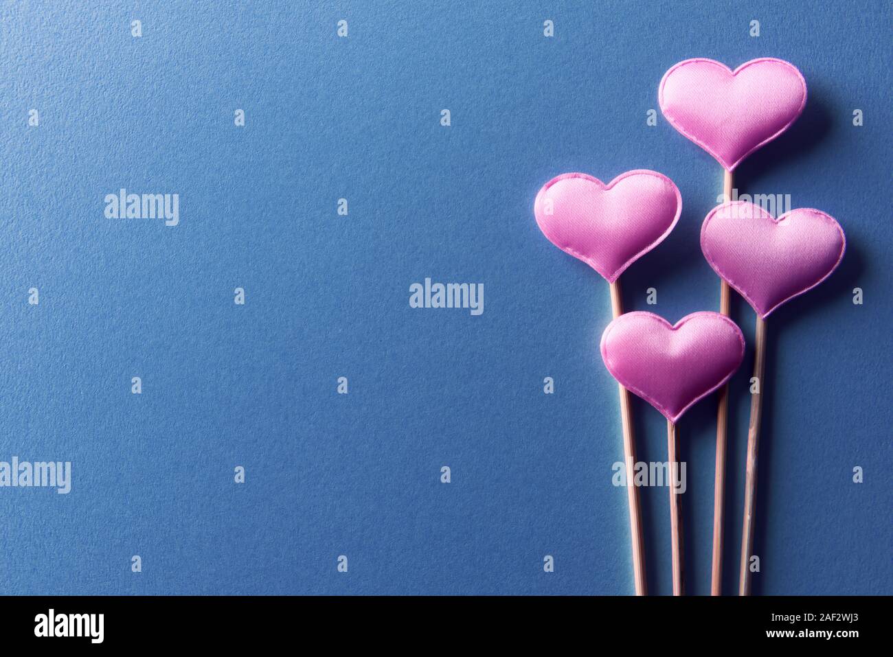 Cuori rosa su bastoni di legno su sfondo blu closeup. Il giorno di San Valentino sfondo, texture creative e il concetto di amore Foto Stock