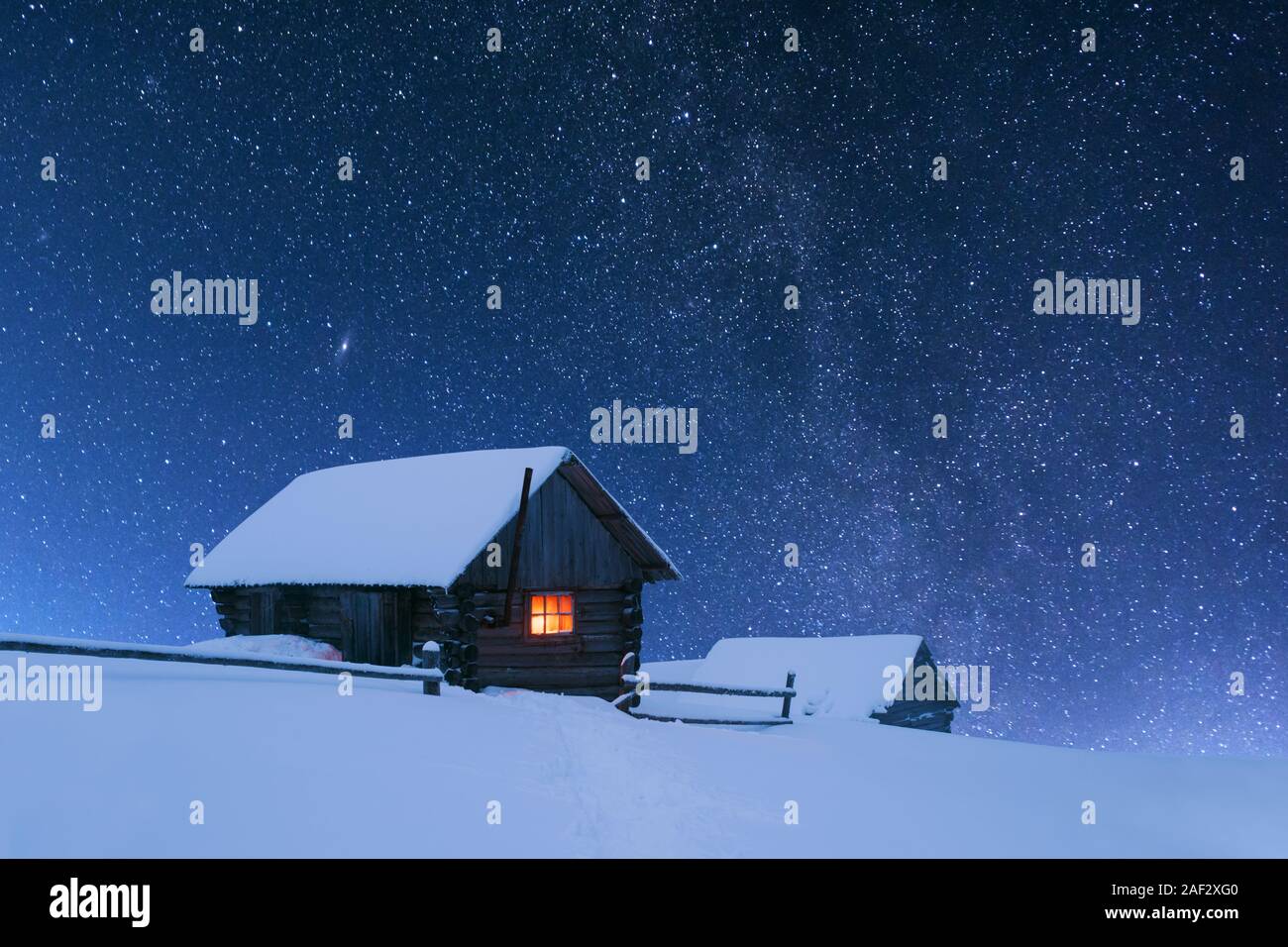 Fantastico paesaggio notturno incandescente dalla via lattea. Drammatica scena invernale con casa innevato con la luce nella finestra . Carpazi, Ucraina, l'Europa. Foto Stock