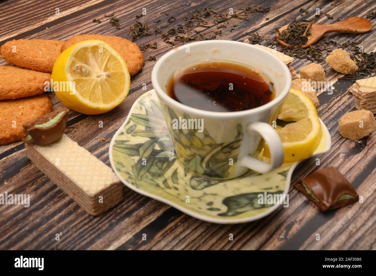 Una tazza di tè nero, spicchi di limone, lo zucchero di canna fette, fiocchi d'avena biscotti, cialde su uno sfondo di legno. Close up Foto Stock