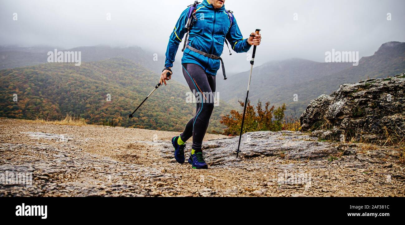 Uomo con pali trekking a piedi il sentiero di montagna in autunno piovoso meteo Foto Stock