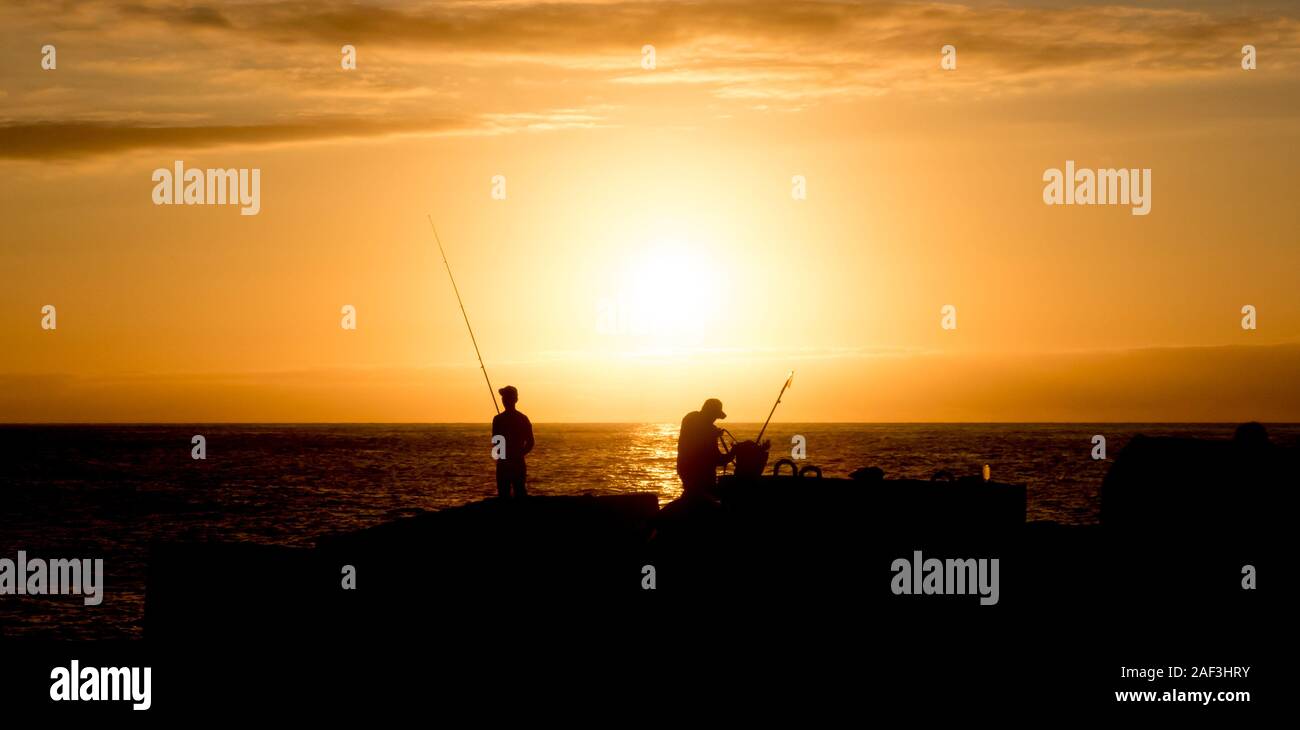 Due pescatori godendo di uno splendido tramonto a praticare il proprio hobby preferito e cercando di prendere la cena home Foto Stock