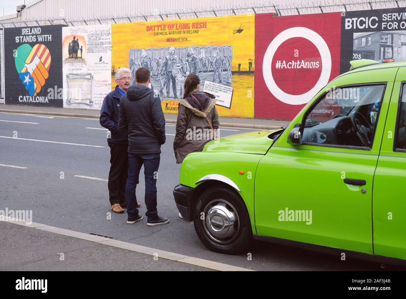 Verde della cabina tradizionale su un tour di Belfast, con driver dando la storia di difficoltà per due turisti di fronte sulla pace art wall Foto Stock