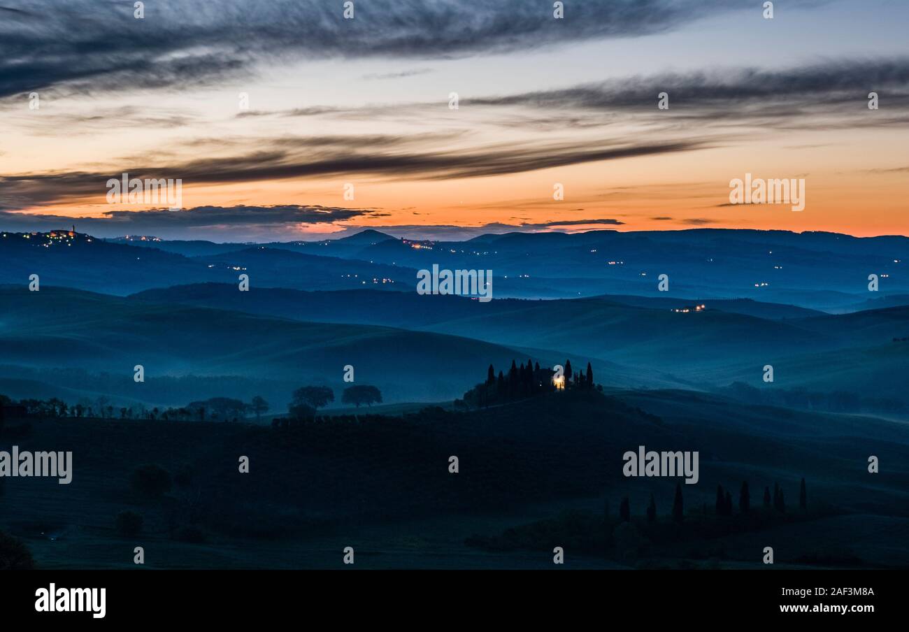 Tipico del territorio collinare della campagna toscana in Val d'Orcia, l'azienda agricola Podere Belvedere su di una piccola collina e la nebbia nelle valli, di sunrise Foto Stock