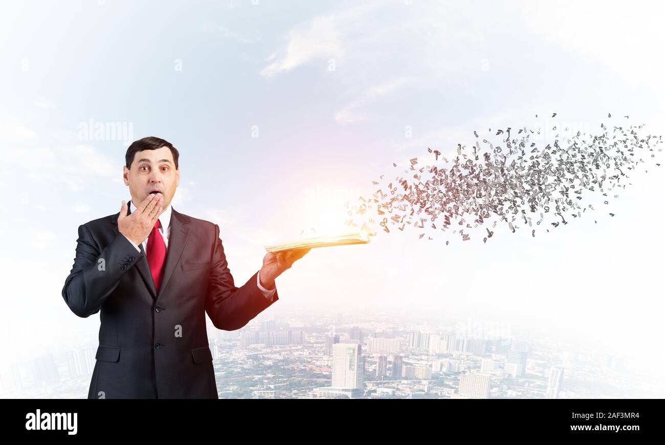 Imbarazzato proprietario che copre la bocca con la mano e azienda libro aperto. Startled uomo nel business suit e tirante permanente sulla città sfondo con battenti Foto Stock