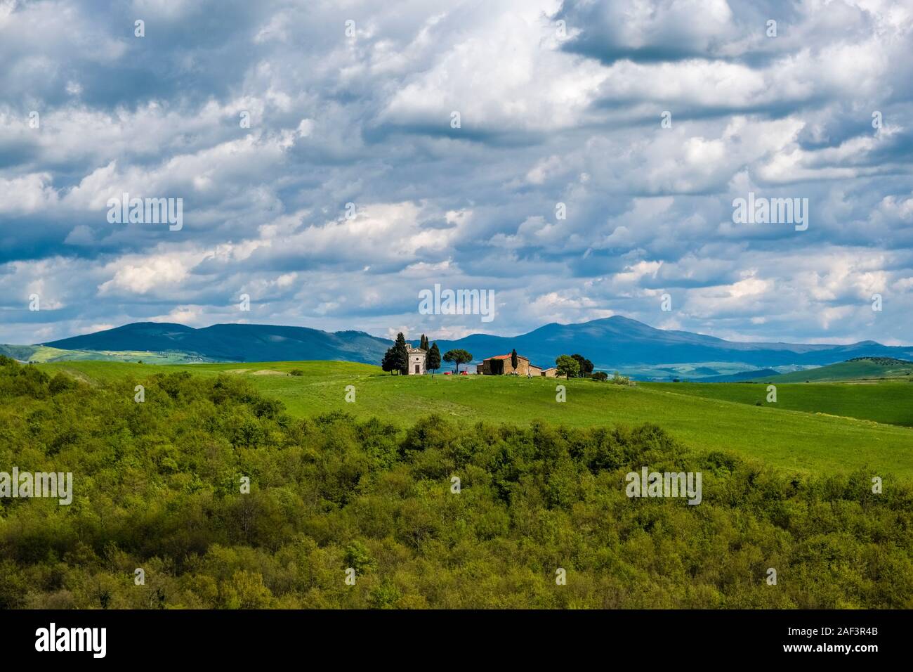 Tipico del territorio collinare della campagna toscana in Val d'Orcia con cielo nuvoloso, cappella di Vitaleta, Madonna di Vitaleta in distanza Foto Stock