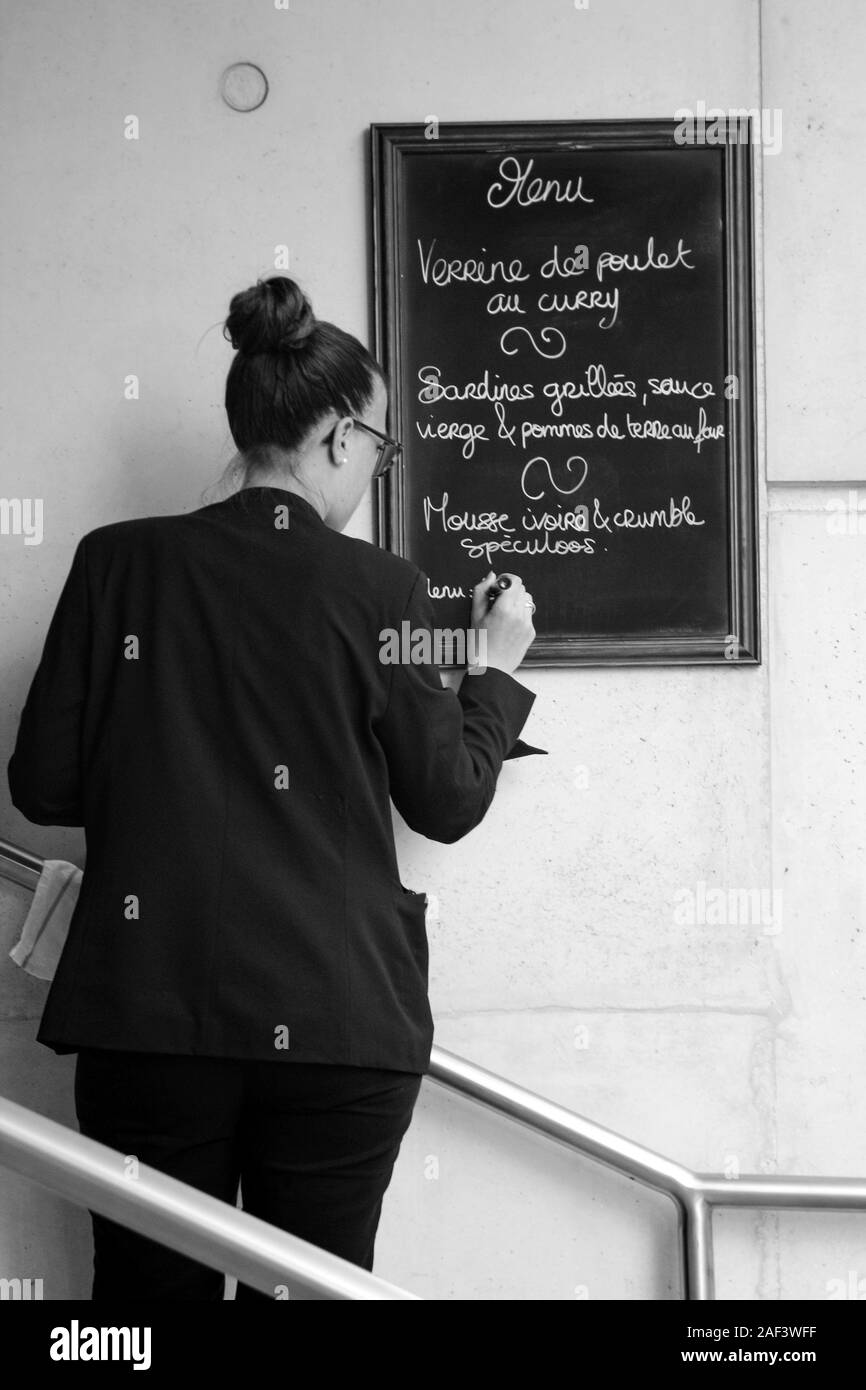 Immagine in bianco e nero di giovane donna iscritto il menu del ristorante sulla lavagna a Parigi, Francia Foto Stock