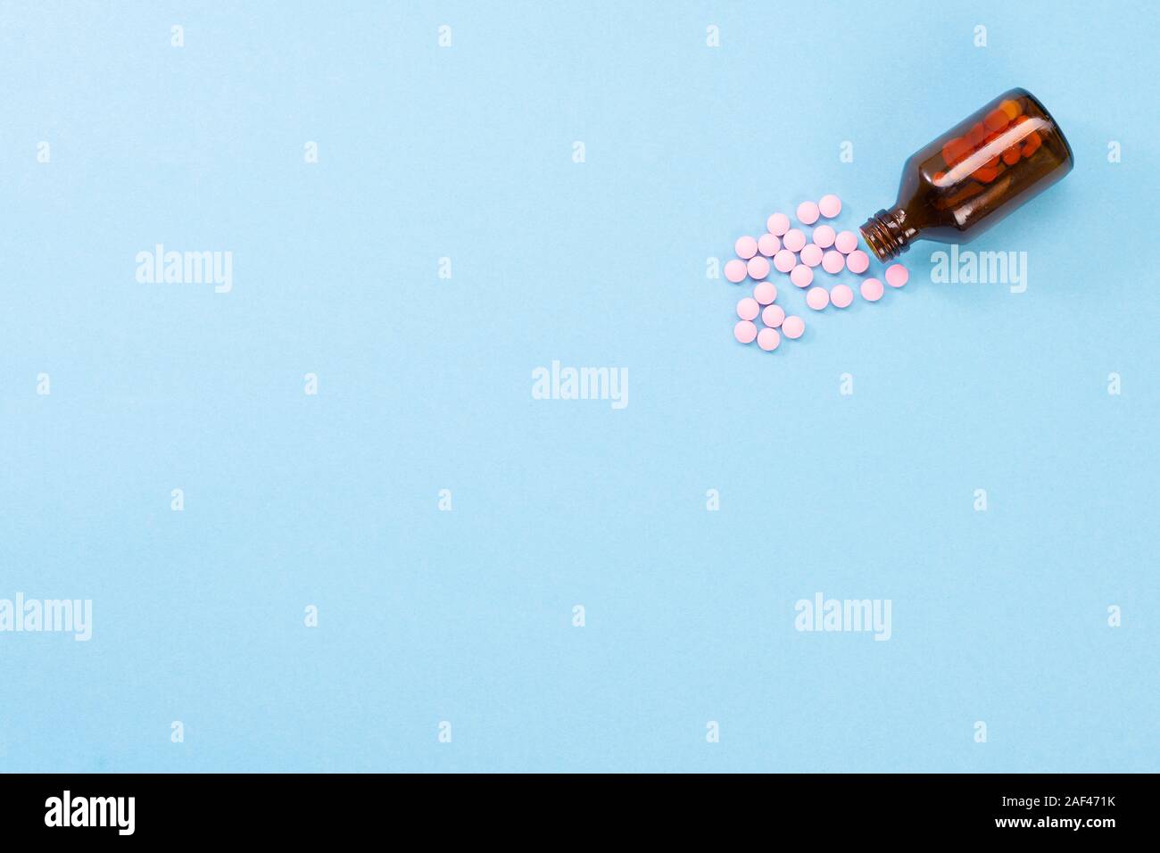 Pillole di rosa e bottiglia di vetro su uno sfondo blu. Il concetto di assistenza sanitaria e di pillole. Flatlay vista da sopra. Copyspace per testo Foto Stock