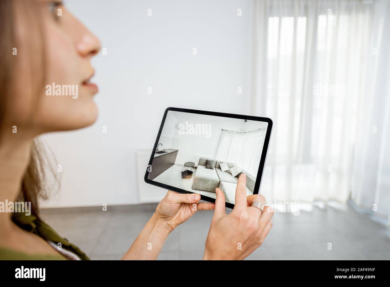 Giovane donna mettendo nuovi mobili su una tavoletta digitale nel vuoto interno, guardando come si guarda prima di acquistare. Concetto di realtà aumentata nel design e retail business Foto Stock