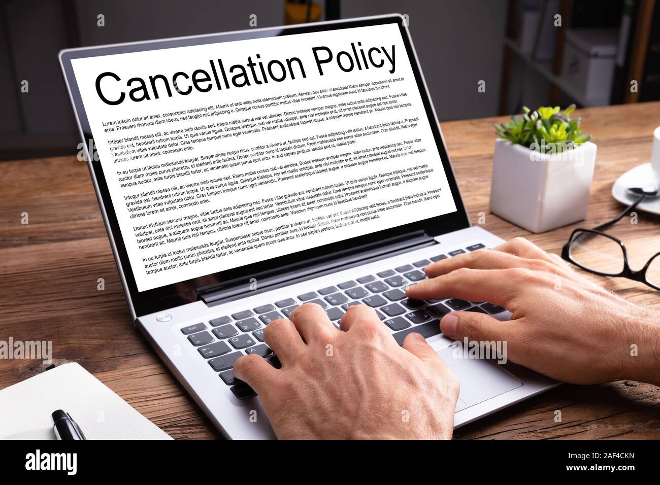 Uomo Accordo di lettura della Politica di Cancellazione su schermo laptop sulla scrivania di legno in ufficio Foto Stock