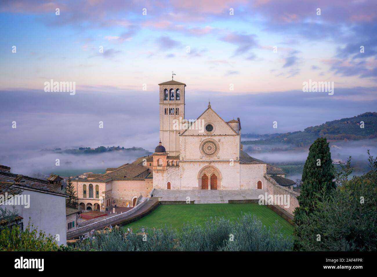 La maestosa Basilica di San Francesco in Assisi, Italia. Fotografato dal di sopra all'alba, tra la nebbia di mattina e il cielo nuvoloso su un giorno d'inverno. Foto Stock