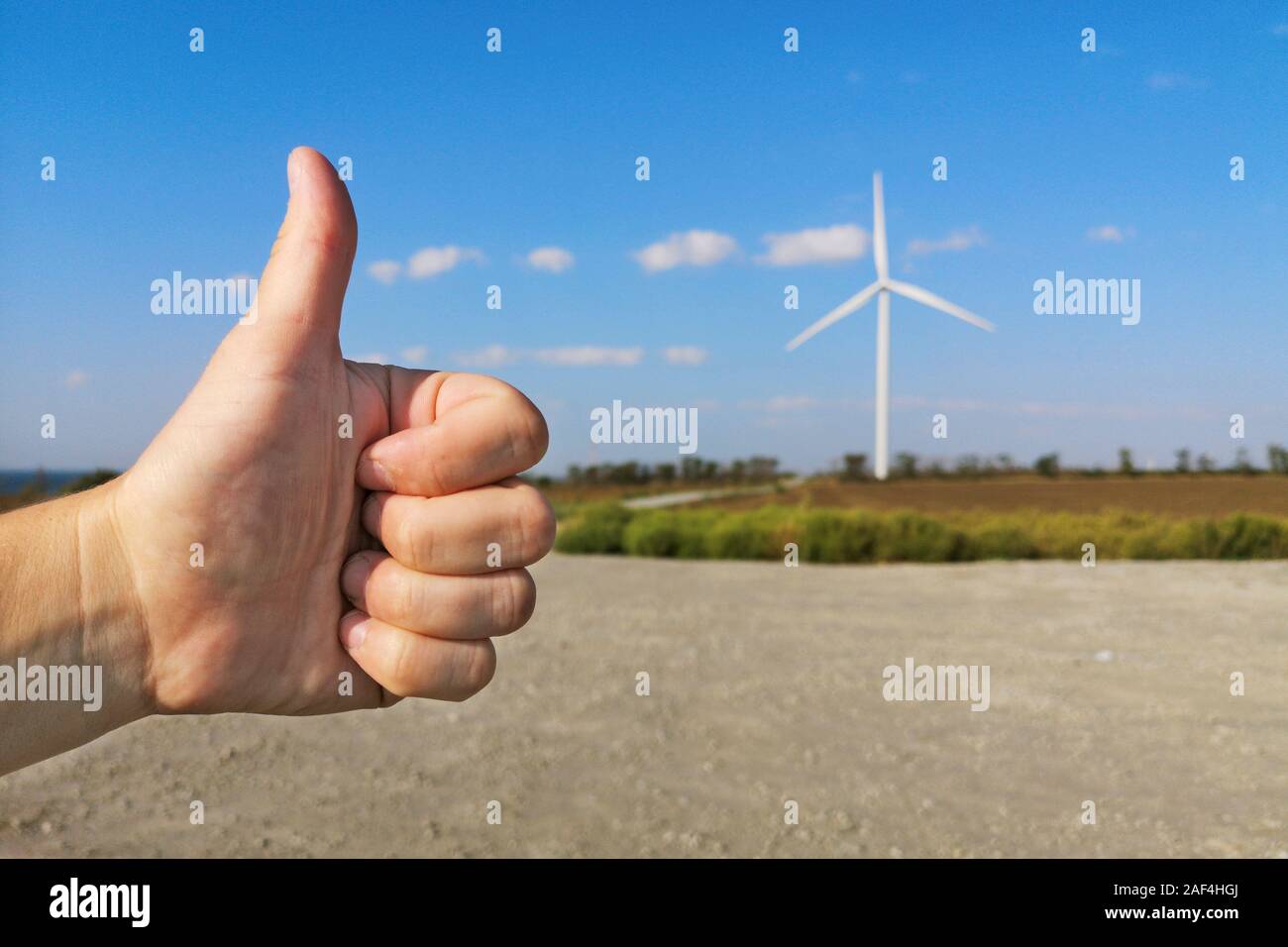 Pollice in alto sullo sfondo delle turbine eoliche e cielo blu. Turbina eolica - fonte di energia rinnovabile. Foto Stock