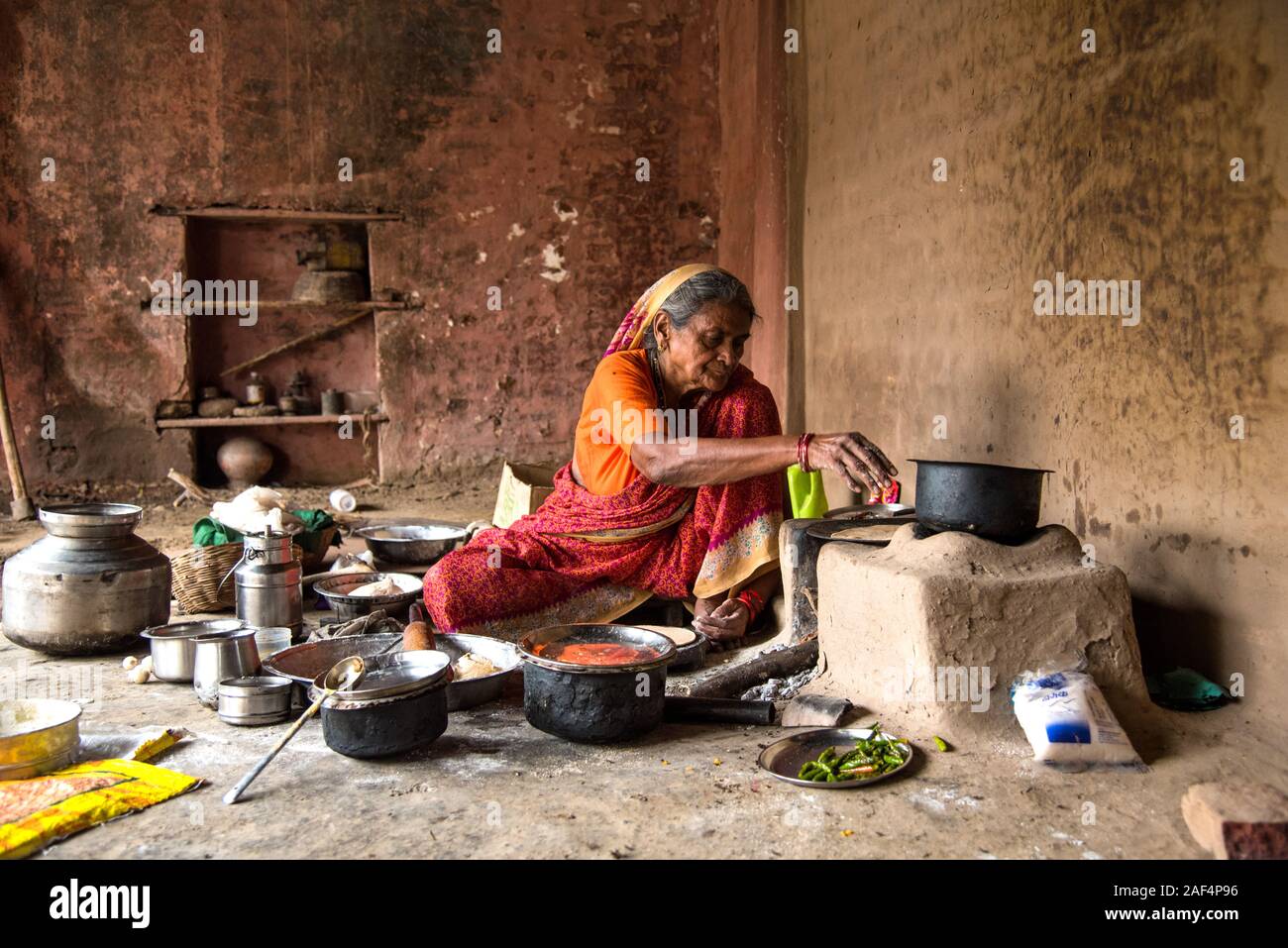 CHIKHALDARA, MAHARASHTRA - Agosto 28, 2018: Un misterioso vecchio donna fare e cucina / cottura di alimenti freschi in un villaggio rurale in una cucina vintage u Foto Stock