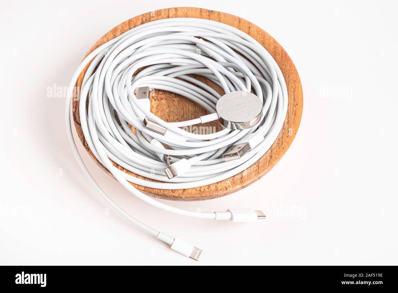 Più bianco Apple cavi di potenza e dei connettori agitando in una ciotola di legno impostato su sfondo bianco. Foto Stock