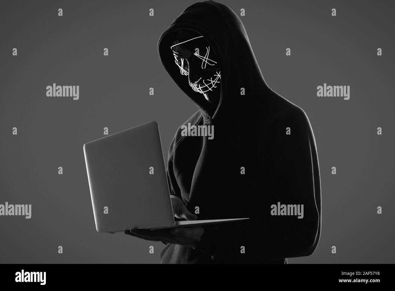 Ritratto di un anonimo uomo in una felpa con cappuccio nero e maschera al neon hacking in un computer. Studio shot. Foto Stock