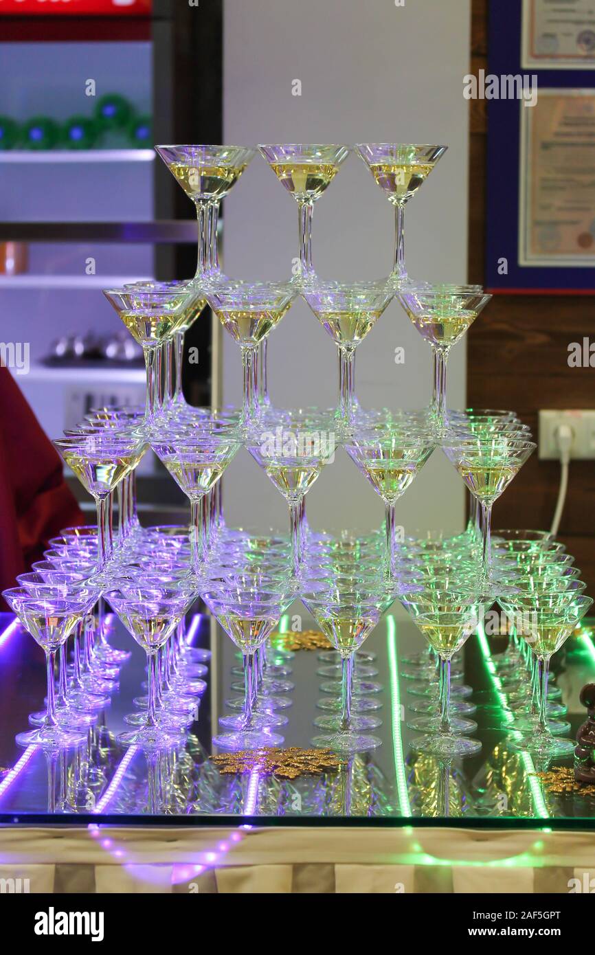 Torre di champagne con quattro file di bicchieri. Evento di celebrazione a parte. Bar decorazione con strisce LED di porpora e di colore verde si accende. Holiday backgroun Foto Stock