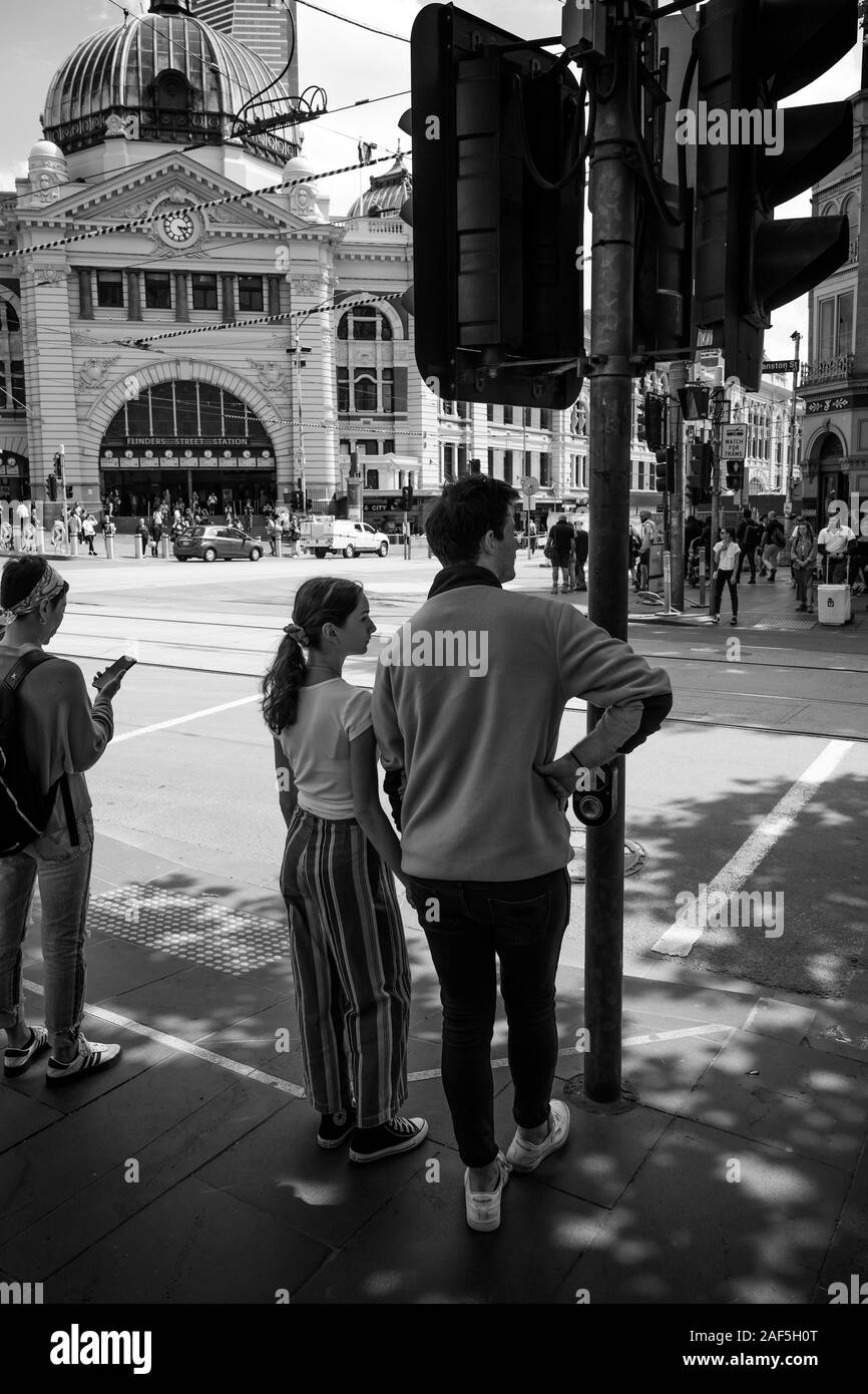 Coppia giovane attendere a croce Swanston Street Melbourne, con la stazione di Flinders Street in background. Foto Stock