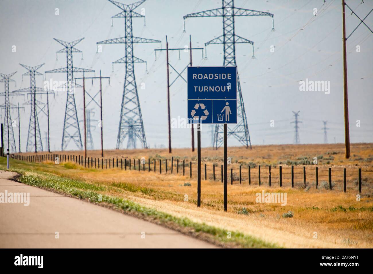 Informazioni su strada segno blu, Strada affluenza alle urne con ordinato uomo, simboli di riciclaggio, canadese paese rurale strada contro tralicci elettrici sullo sfondo Foto Stock