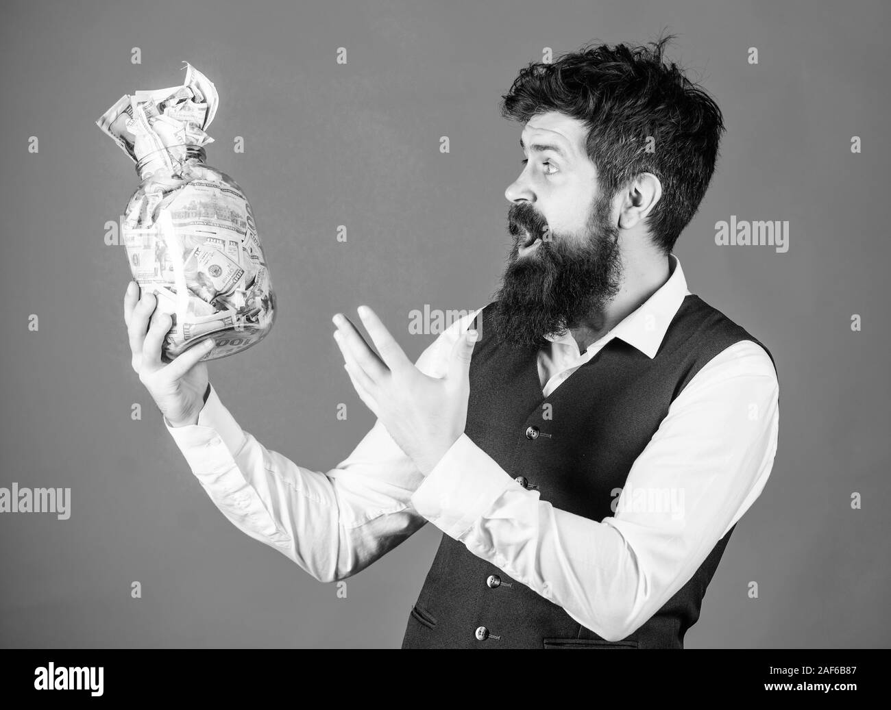 Guadagnando denaro contante per il suo lavoro. Imprenditore entusiasta holding jar con denaro contante. Uomo Barbuto mantenendo la tesoreria. Il flusso di cassa di bilancio. Foto Stock