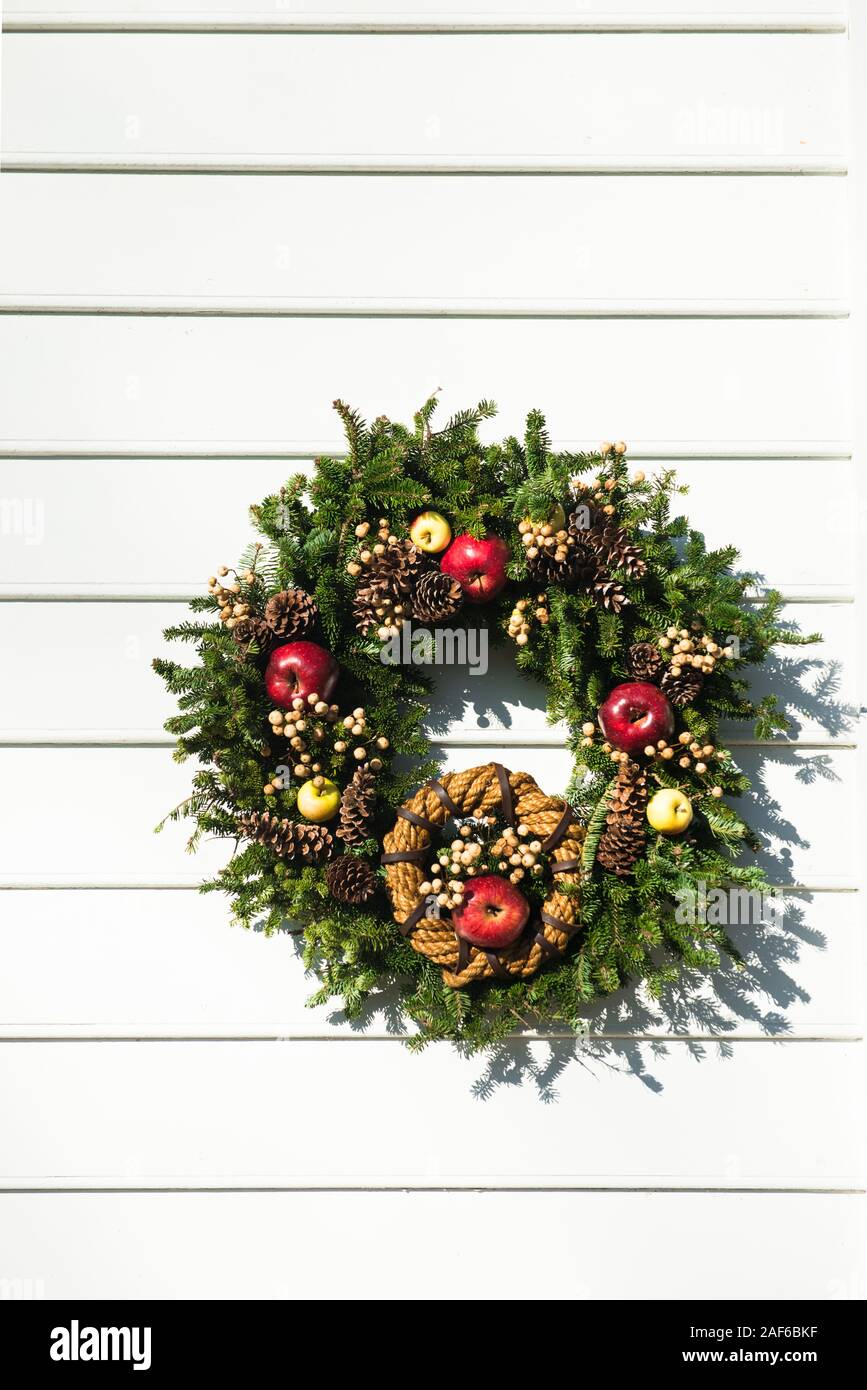 Simmetriche ghirlanda sempreverde con minore corda intrecciata-corona, rilegati in pelle. Colonial Williamsburg. Il rosso e il giallo mele, pigne, bacche di colore bianco. Foto Stock