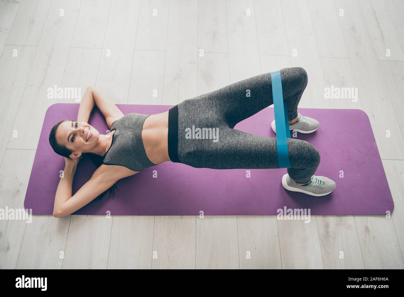 Parte superiore al di sopra di un angolo alto foto di gioiosa attivo ragazza sportive giacciono sul tappetino viola la pratica di asana sport esercizio ponte fanno sollevare le ginocchia con espansore di blu Foto Stock