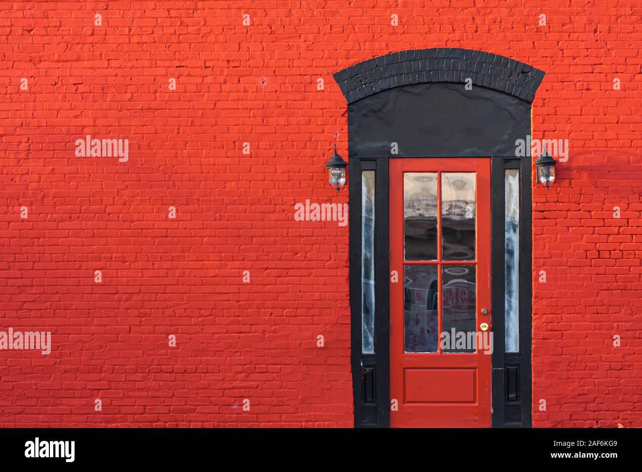 Un rosso brillante porta con telaio nero su un muro rosso. Foto Stock