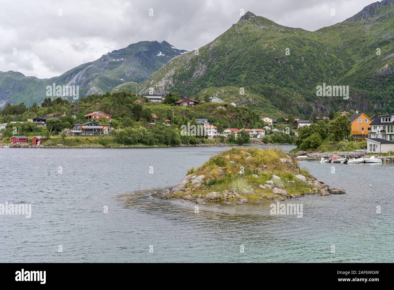 Cliff e distanziati tra loro case a fiordo di artico ingresso verde , girato sotto la luminosa luce nuvoloso vicino a Svolvaer, Austvagoya, Lofoten, Norvegia Foto Stock