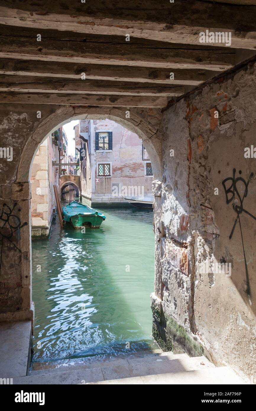 Visualizza in basso un pittoresco canale posteriore dal sotto sottoportego o passerella coperta di Calle de Mezo, Santa Croce, Venezia, Veneto, Italia Foto Stock