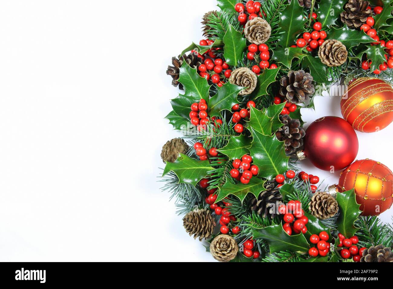 Colorato naturale tradizionale holly ghirlanda di Natale con baubles e bacche rosse per celebrare la stagione delle vacanze isolato su bianco con spazio di copia Foto Stock