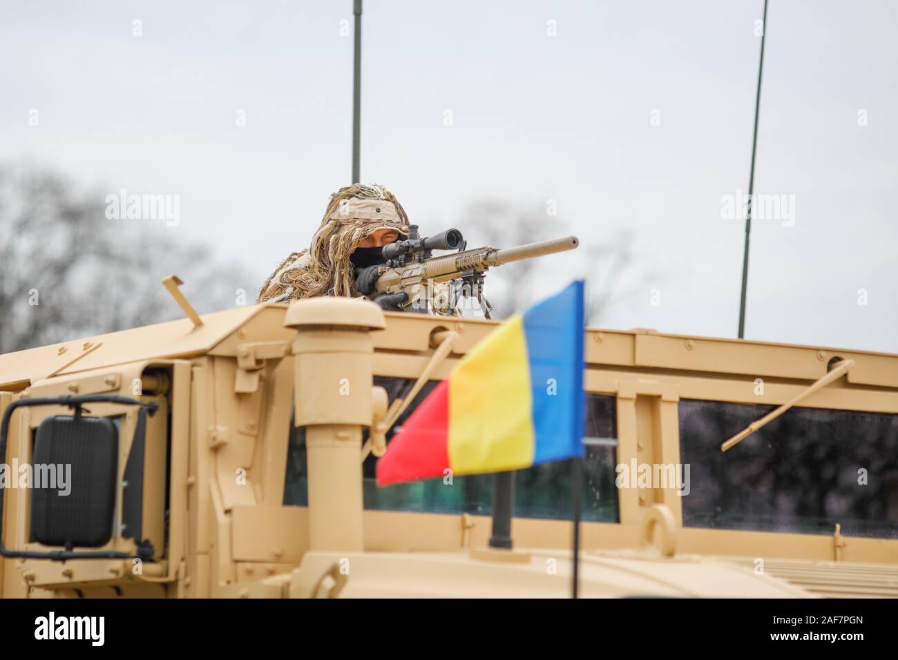 Bucarest, Romania - 1 Dicembre 2019: romeno army sniper vestito in una Ghillie Suit detiene una M110 fucile da cecchino sulla parte superiore di un Humvee veicolo blindato dur Foto Stock