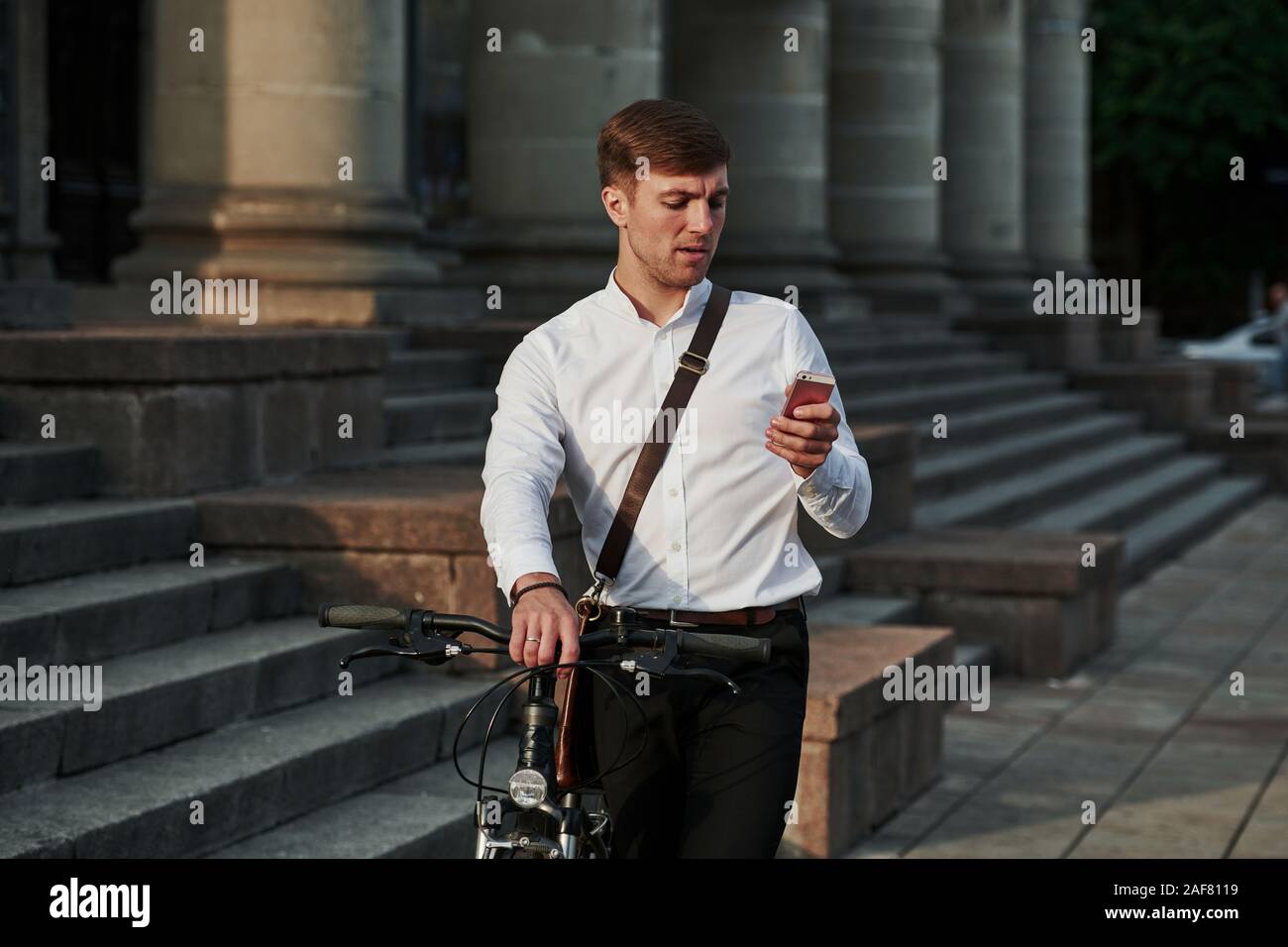 Hai bisogno di chiamare un direttore generale. Imprenditore in abiti formali con nero è in bicicletta in città Foto Stock