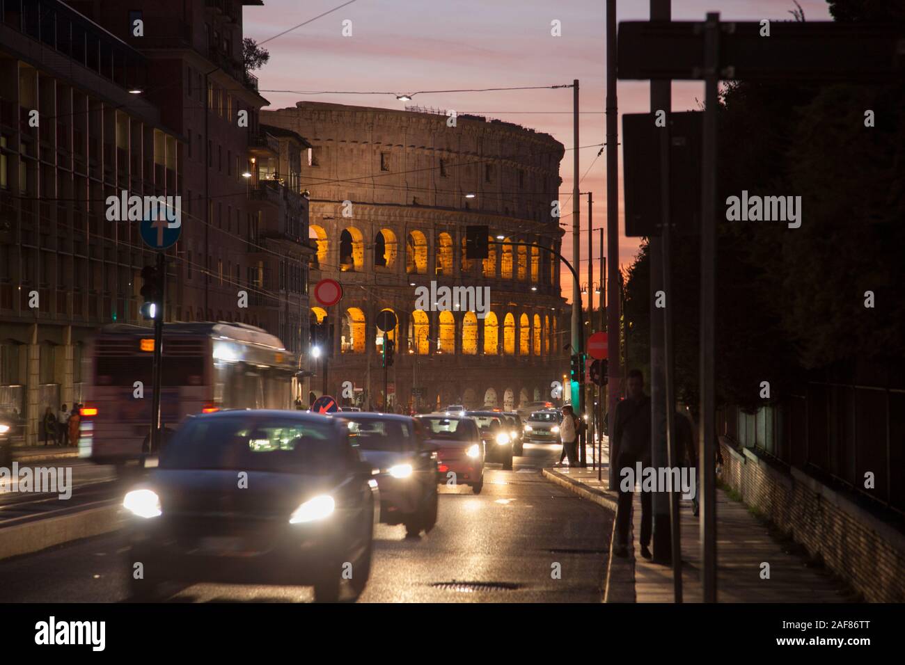 La parte esterna del Colosseo di Roma con le vetture a motore durante un rush hour tramonto Foto Stock