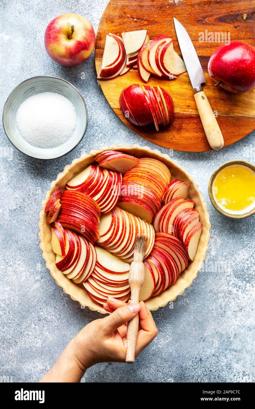 Preparazione di una crostata di mele.Pennellato a mano le mele a fette con burro fuso Foto Stock