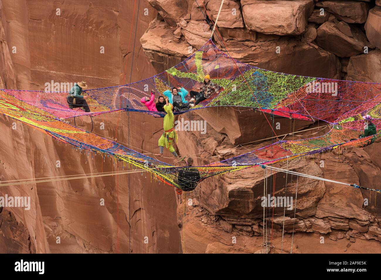 Un giovane uomo slacklining o highlining sullo Space Net a centinaia di metri di altezza sopra il Canyon minerali nei pressi di Moab Utah durante un raduno highline come il suo amico Foto Stock