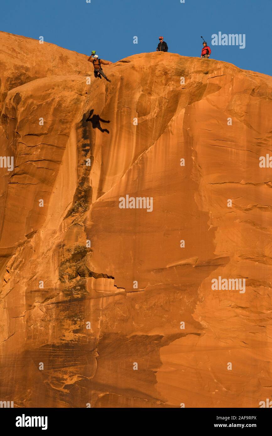 Un ponticello di base salta fuori dalla parte superiore del piede 400 faccia verticale dell'oggetto contrassegnato per la rimozione definitiva in Kane molle Canyon vicino a Moab, Utah. Nota la sua ombra sulla scogliera. Foto Stock
