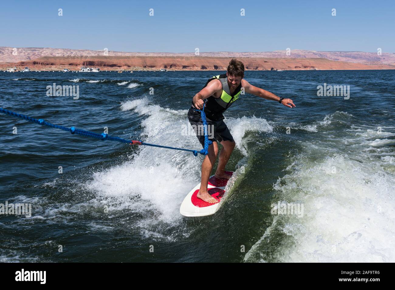 Un giovane uomo wake surf dietro una barca sul Lago Powell in Glen Canyon National Recreation Area nel sud dello Utah, Stati Uniti d'America. Foto Stock