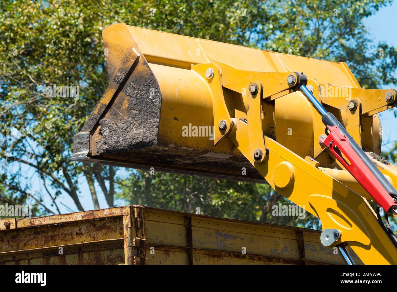 Scavatrice o benna di un escavatore o pala sollevata al di sopra di un carrello o camion durante la costruzione, il concetto di industria di costruzione di macchinari Foto Stock