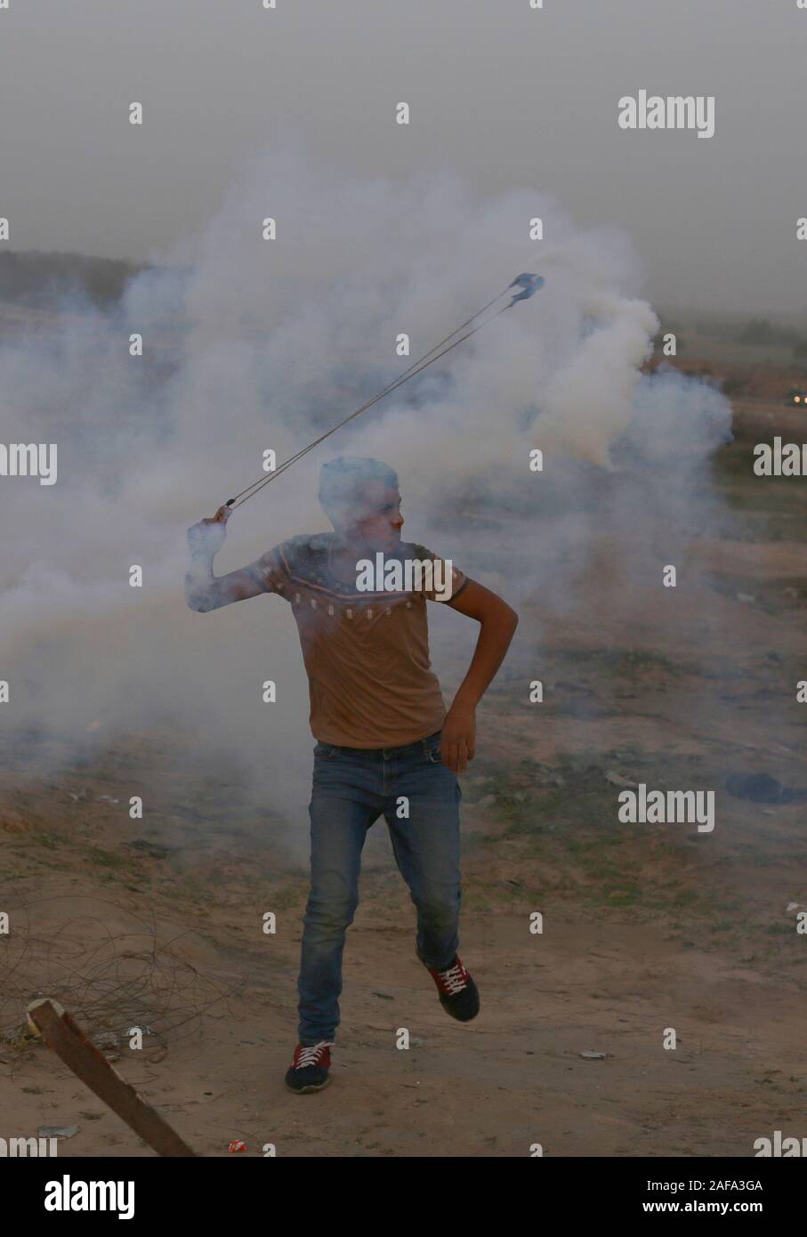 La striscia di Gaza. Xiii Dec, 2019. Un manifestante palestinese utilizza un slingshot a lanciare indietro una lacrima bombola del gas sparati dalle truppe israeliane durante scontri nella zona centrale della striscia di Gaza, Dic 13, 2019. Credito: Khaled Omar/Xinhua/Alamy Live News Foto Stock