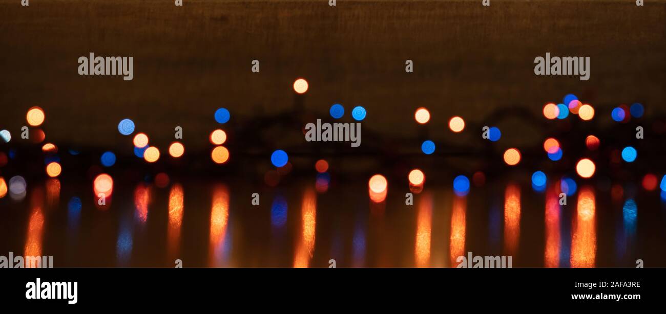 Le luci di Natale incandescente. Vacanze di Natale decorazione sfondo, banner. Colorata ghirlanda di luci accese, riflessioni sul pavimento Foto Stock
