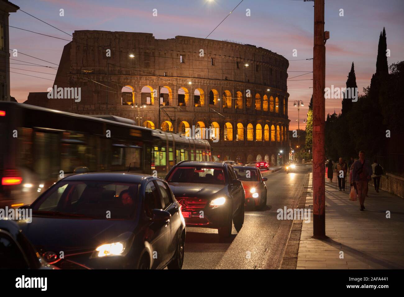 La parte esterna del Colosseo di Roma con le vetture a motore e un tram in ora di punta Foto Stock