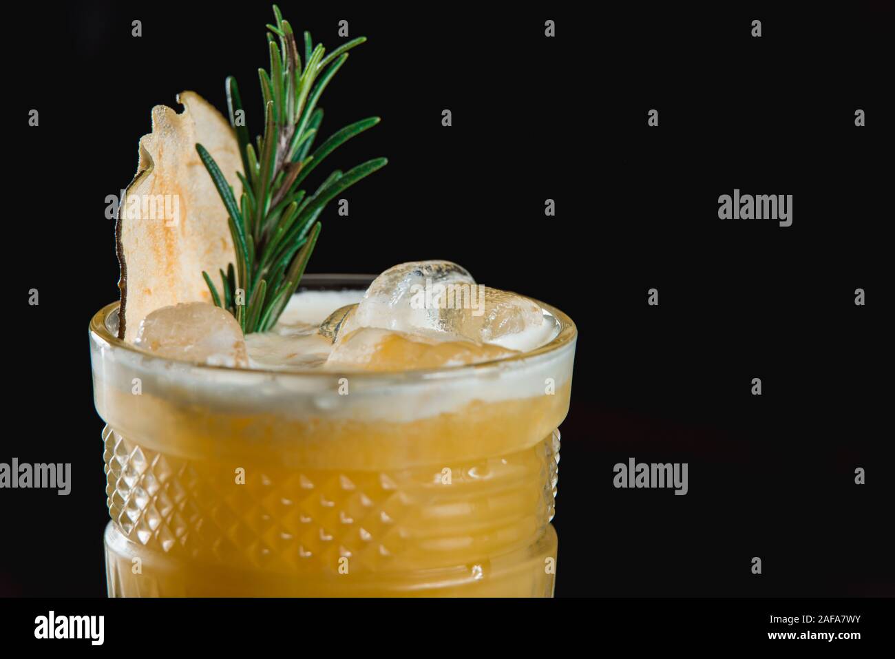 Il freddo Whiskey Sour cocktail con ghiaccio e chip di Apple e un pezzo di timo sulla parte superiore. La metà di un limone vicino al vetro Foto Stock